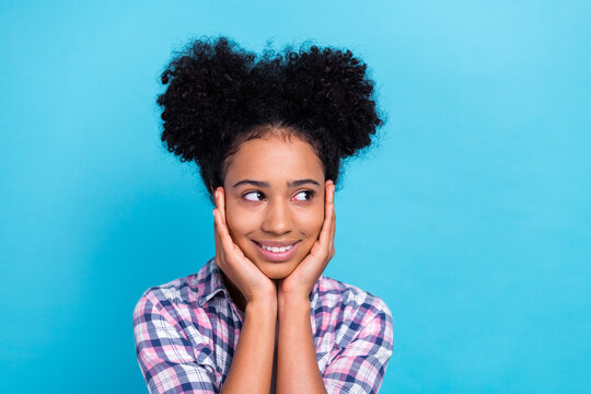 Portrait of optimistic pleasant teenager afro hair plaid shirt arms on cheekbones look empty space isolated on blue color background