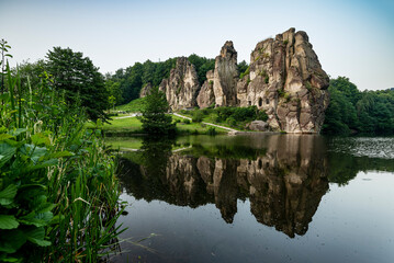 Fototapeta na wymiar Scenic view of the Externsteine stones over the calm water of the nearby pond, Teutoburg Forest, Germany
