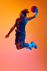 Full-length image of young sportsman, basketball player in motion, jumping with ball against orange...