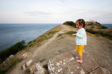 Cute little girl standing on top of a cliff and looking at the sea. Cape Emine, Black sea coast, Bulgaria.
