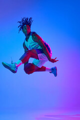 Fototapeta na wymiar Competitive, ambitious sportsman, young basketball player in motion with ball against gradient blue background in neon lights. Concept of professional sport, competition, hobby, game, competition, ad