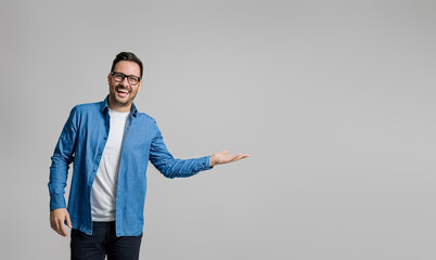 Portrait of cheerful handsome businessman showing and advertising new product on gray background - Powered by Adobe