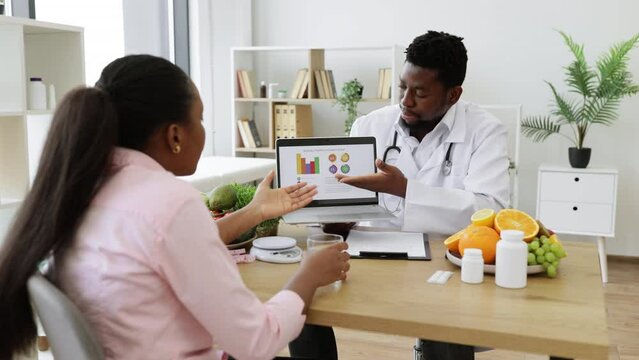 Female patient with long ponytail visiting doctor in private polyclinic. Experienced food expert in white medical uniform and stethoscope analyzing treatment effectiveness using graphs on laptop.