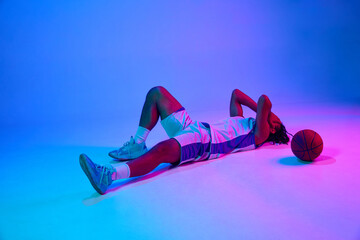 Loosing game. Young guy, basketball player lying on floor in sadness against gradient blue...