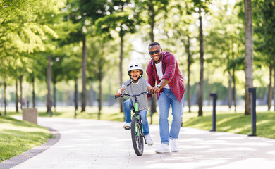 Happy ethnic family father teaches child  son  to ride bike in park - 625204769