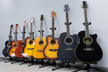 Acoustic guitars of different sizes and colors on the stands in the musical instrument store