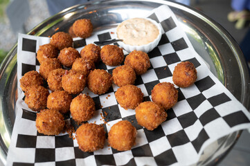 silver platter of fried round hushpuppies served on black and white checkered paper with dish of horseradish aioli, at cocktail hour at outdoor wedding