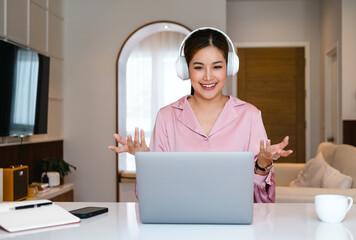 Smiling asian woman freelancer wearing headset communicating with client via video computer call....