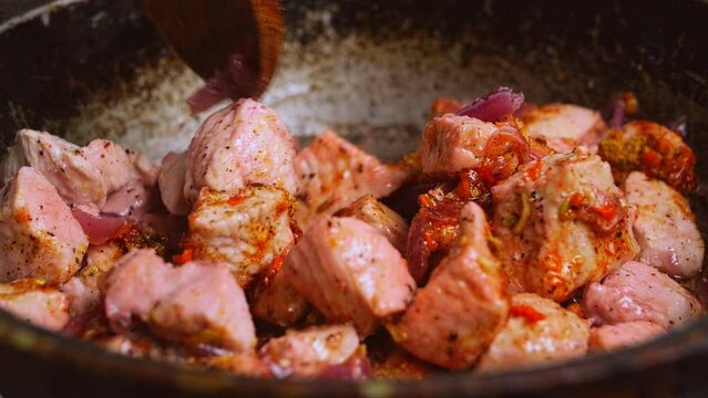 Chicken in spices with sumac for cholent is stirred in a pan with a wooden spatula. Medium plan.