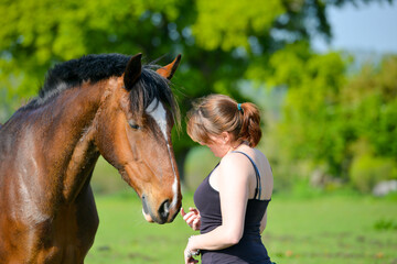 Close up shot of pretty young woman and her beautiful bay horse sharing a loving  moment of friendship as they stand together in English countryside on a summers day.