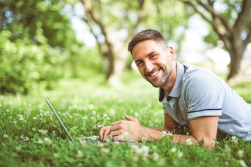 Happy cheerful man with a laptop outdoors in nature, freedom and happiness concept