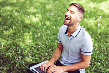 Naklejka na ściany i meble Happy cheerful man with a laptop outdoors in nature, freedom and happiness concept