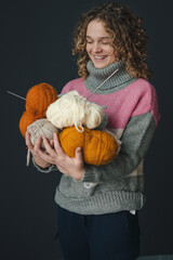 Curly haired woman smiling while posing over isolated background holding balls of yarn and knitting...