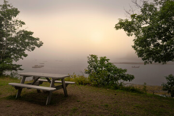 Fototapeta na wymiar Foggy morning seascape with empty bench and table on the green hill at Boothbay Harbor in Lincoln County, Maine