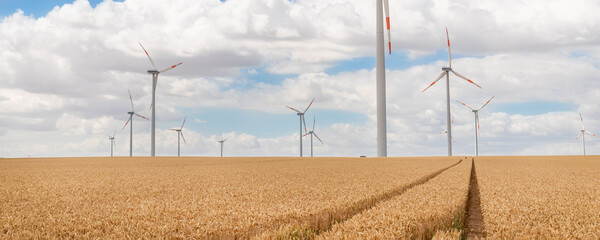 Scenic landscape view of wheat field harvest and big modern wind turbine mill farm against...