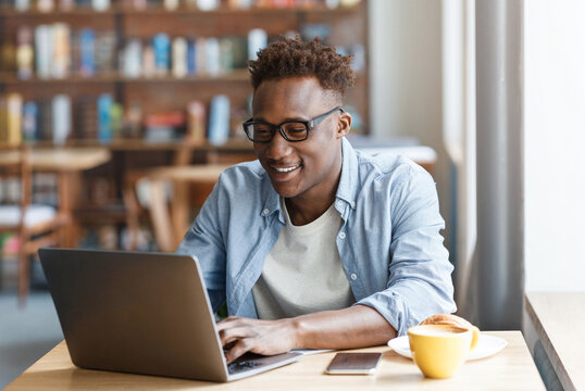 Positive millennial black guy working online at cafe