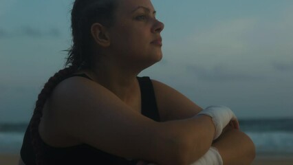 Female boxer MMA fighter raises head confidently on beach. Close up.