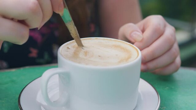 Woman hand stiring cappuccino coffee in a cup with teaspoon.