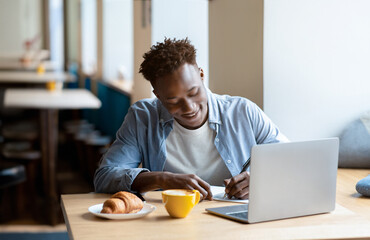 Fototapeta na wymiar Happy black man studying remotely on laptop at city cafe