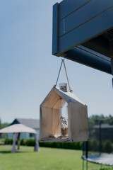 Modern bird house (with bird feeder in middle) made of light wood hanged on side of garage in domestic area