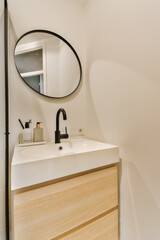 a modern bathroom with white walls and wood cabinetry, including a round mirror on the wall above the sink