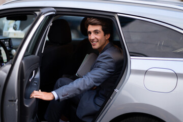 Cheerful young man entrepreneur getting into auto