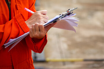 Action of a safety officer in full PPE coverall is writing note on paper document during perform...