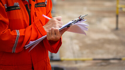 Action of a safety officer in full PPE coverall is writing note on paper document during perform...