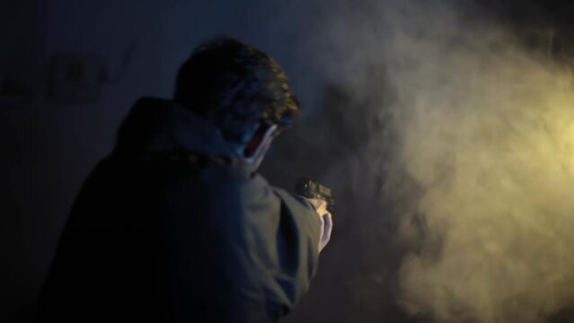 Backside shot of an officer trained professional with a gun walking with some smoke in the background, dramatic lighting. HD footage of a man walking. Soldier with pistol.