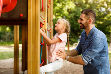 Girl spending time on playground, dad helping daughter climbing the stairs, enjoying time together in the park