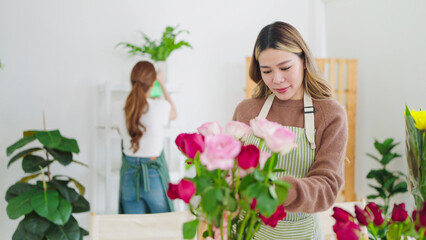 Young asian woman florist in apron working in flower shop. Concentrated young female florist arranging flowers in shop. Small business concept