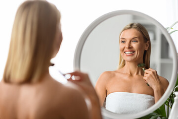 Obraz na płótnie Canvas Beauty Treatments. Smiling Mature Woman Using Greenstone Jade Roller At Home