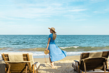 A beautiful young woman with long blond hair in a long blue dress walks along the beach. girl in a blue dress. Long red dress fluttering in the wind