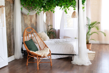 Interior boho design bedroom with garland flowers and plants. Cozy light bedroom in Scandinavian style bedroom, canopy bed and  wicker rattan armchair. Bed decorated flowing white curtains canopies.  © stock_studio
