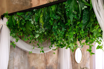 Composition from garland flowers and plants on wall. Ceiling decoration. Wall with curly green plants garlands hanging from ceiling. Herb and plant wall, nature wall. Interior wedding party decor. - obrazy, fototapety, plakaty