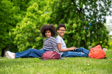 Naklejka na ściany i meble Two curly-haired teens sitting on the grass in the park and feeling good