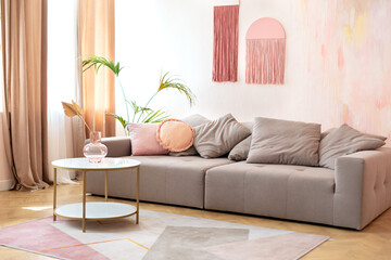 Cozy living room interior design with stylish grey sofa, pillows and coffee table with bouquet of dried flowers in modern scandinavian home. Modern room interior with comfortable sofa and furniture