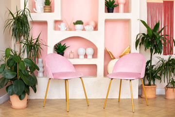 Modern composition of wabi sabi interior with arch shelf with home decoration and pink chairs. Stylish interior of living room and panel macrame on wall. Houseplants in terracotta pots at home 