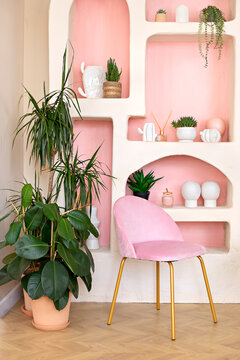 Modern composition of wabi sabi interior with arch shelf with home decoration and pink chair. Stylish interior of living room and panel macrame on wall. Houseplants in terracotta pots at home	