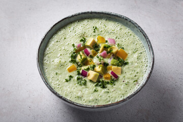 Green cucumber gazpacho cold cream soup styled and decorated in rustic bowl with ingredients on gray table, top view