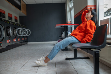 Tired bored woman sitting in automatic laundry room while waiting for the laundry to be done.