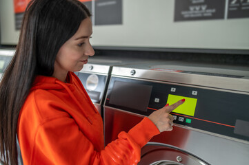 Fototapeta na wymiar Young woman pressing button in washing machine at public laundry.