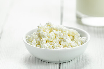 Saucer with cottage cheese and a glass of milk on a white wooden table. Rustic style