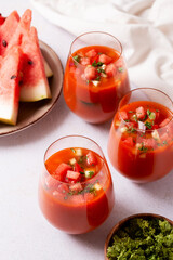 Spanish tomato and watermelon gazpacho cold soup styled and decorated in glasses with ingredients on white table, top view