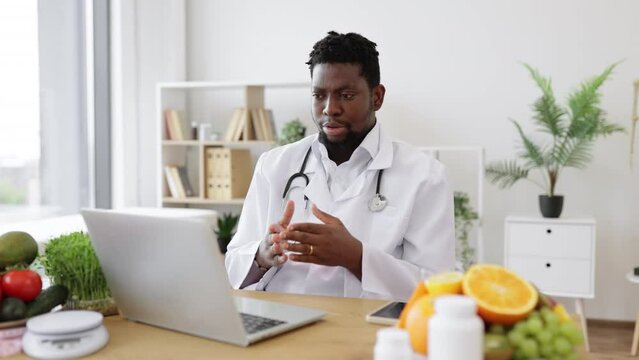 African american nutrition specialist holding online consultation with patient using wireless laptop in medical clinics. Male doctor dressed in white lab coat telling about importance of healthy diet.