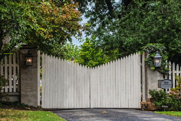 White picket electric gate entrance to estate with mailbox and packages hidden behind bushes and no...