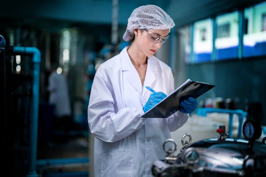 Factory worker checking water bottles in the warehouse at the industrial factory. Female worker recording data at the beverages manufacturing line production. - Powered by Adobe
