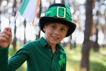 Happy little leprechaun celebrating St Patricks Day. Portrait of a cute white kid waving with flag...