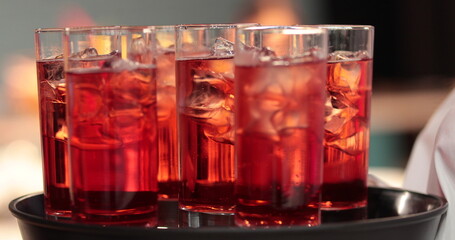 A tray with many glasses with drinks. Red drinks are delivered by a waiter.