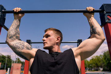 portrait of a young sweaty sportsman doing horizontal bar swings arms and shoulders push-ups on the sports ground during street training
